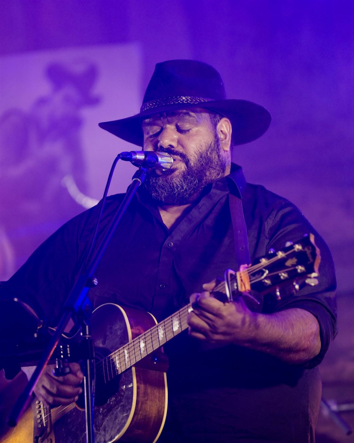 Bradley Hall singing with his acoustic guitar under purple stage lights